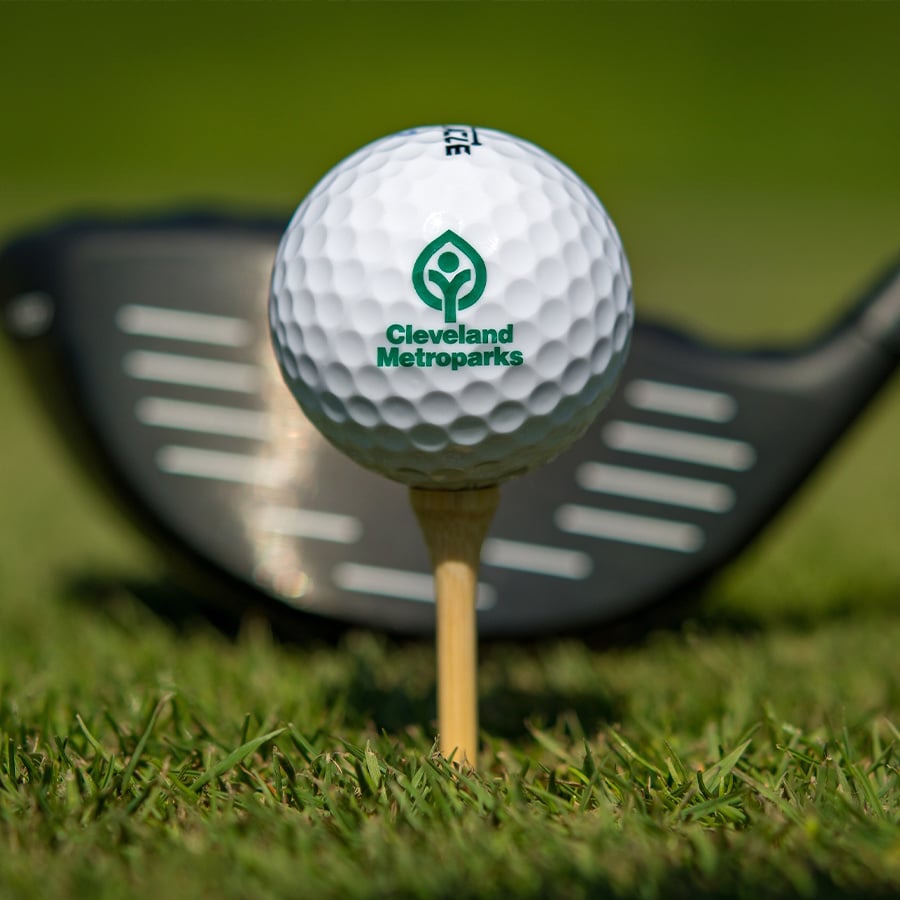 close-up of a golf ball with the Cleveland Metroparks logo on it and a golf club in the background
