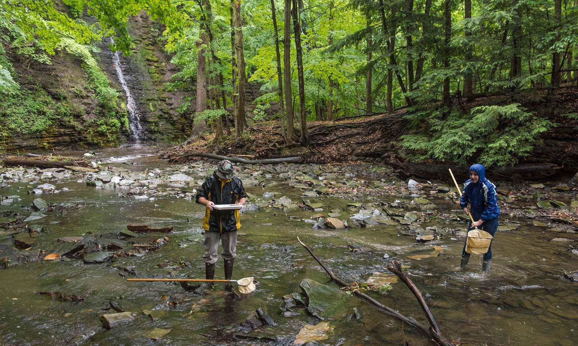 Two people standing over land with water flowing